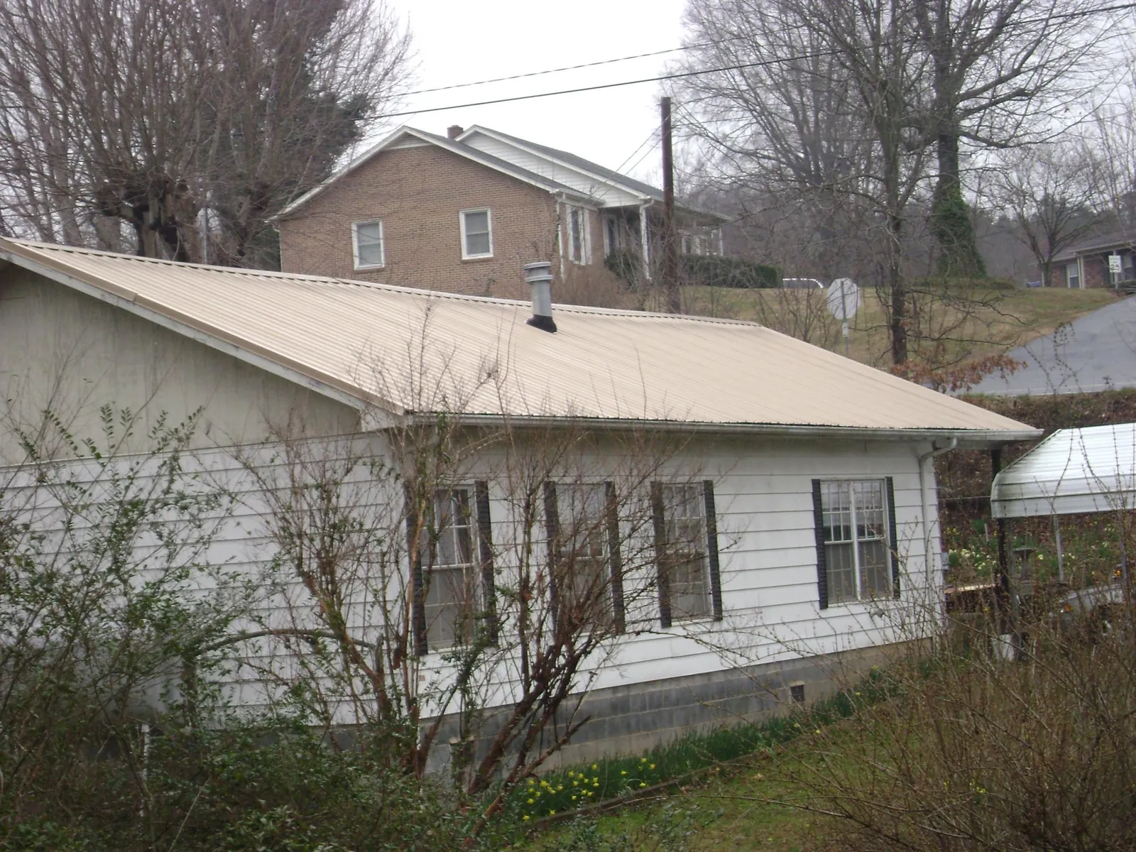 Tan metal roof on a white sided house set into a hillside — Commercial Roofing by Roofing Brothers in Egg Harbor City